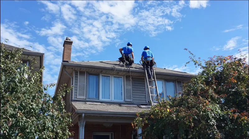 Two workers installing eavestroughing on a two-storey house.